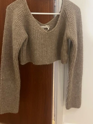 Beige cropped stickad tröja Gina Tricot - Cropped stickad tröja från Gina Tricot i en mjuk beige nyans. Tröjan har v-ringning, långa ärmar och ribbstickad struktur. Perfekt för lager-på-lager och en trendig look. Är inte säker på storleken men passar mig som har xs och S
