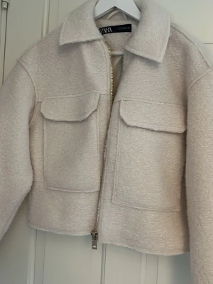 Beige teddy cardiganjacka från Zara - Mysig beige Teddy från Zara i teddy-material. Jackan har två stora bröstfickor med lock, dragkedja framtill och klassisk krage. Perfekt för lager-på-lager och ger en trendig look till din outfit. Den är aldrig använd 