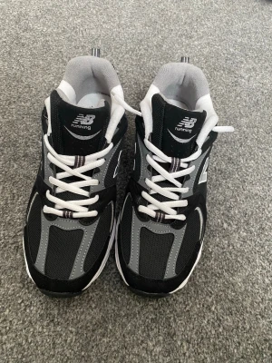 New Balance 530 svarta sneakers - Svarta och grå New Balance 530 sneakers med vita detaljer och vit sula. Klassisk mesh och syntetmaterial, tydlig N-logga på sidan och ABZORB-dämpning i sulan. Perfekta för en sportig och trendig look.