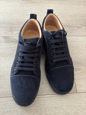 Mörkblå sneakers från Louboutin - Snygga mörkblå sneakers från Christian Louboutin med ovandel i mocka och klassisk låg siluett. Skorna har matchande mörkblå snörning och ljusbeige innersula med guldlogga. Perfekta för dig som gillar stilrena och exklusiva sneakers.