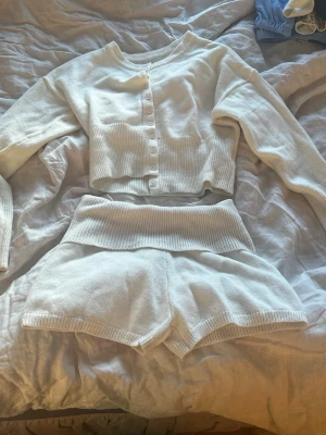 Vit ribbad loungewear-set - Mysigt loungewear-set i vitt med ribbade detaljer. Setet består av en långärmad, croppad kofta med knappar framtill och matchande shorts med bred, ribbad midja. Perfekt för chill dagar hemma.