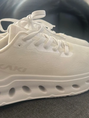 Okaki sneakers i storlek 38 - Säljer ett par vita löparskor från Okaki Mile i storlek 38. I ny skick bara provade inomhus. Skorna har snörning framtill och en mönstrad sula. Mile är  modern löparsko med specialdesignade hål i yttersulan som ökar och optimerar dämpningen. Denna modell har ett ovansida i textil och kommer med praktiska snören i nylon. Det gör att passformen är luftig, lätt, mjuk, flexibel och ger en optimal anpassning till foten. Ny pris 1599kr