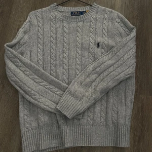Grå stickad tröja från Ralph Lauren - Kabelstickad grå tröja från Polo Ralph Lauren. Perfekt för våren och en snyggare look. Kontakta för fler bilder och pris kan diskuteras.