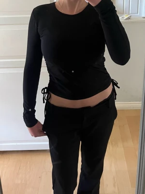 Svart långärmad topp med snörning - Svart långärmad topp med rund halsringning och snygga snörningsdetaljer i sidorna som ger en croppad look. 