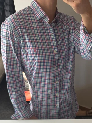 Rutig skjorta från Polo Ralph Lauren - Rutig skjorta från Polo Ralph Lauren i bomull med klassisk krage och knäppning framtill. Skjortan har lång ärm och mönster i blått, rosa, grönt och vitt. Perfekt för en stilren och avslappnad look. Lite missfärgad i kragen, därav priset, annars bra skick 
