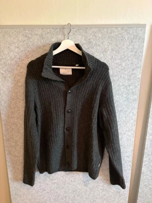 Mörkgrå stickad kofta / cardigan med krage - Mysig mörkgrå stickad kofta från Jack and Jones med krage och knäppning framtill. Koftan har ribbstickat mönster och långa ärmar, går gärna ner i pris vid snabb affär. Passar upp till 185