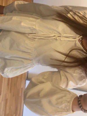 Vit blus med knytning och volang - Söt vit blus med knytning framtill och volang nedtill. Blusen har långa puffiga ärmar och är tillverkad i ett lätt bomullsliknande material. Perfekt att styla med jeans för en trendig look.