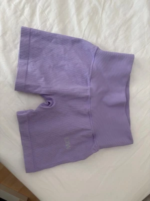 Lila ribbade shorts från ICANIWILL - Säljer ett par lila ribbade shorts från ICANIWILL med hög midja. Perfekta för träning eller chill dagar. Stretchigt material som sitter skönt och följer kroppen. Diskret logga på benet. Supersnygga och trendiga shorts!