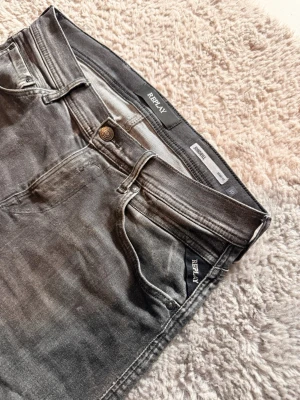 Replay grå slim fit jeans - Säljer ett par grå slim fit jeans från Replay med snyggt slitna detaljer och klassisk femficksdesign. Jeansen har en modern passform och är tillverkade i stretchigt material som ger en bekväm känsla. Perfekt för dig som gillar en stilren look.            Jeansen har en näst intill osynlig röd fläck på högra bakficka. Fläcken finns där men syns inte i allmänheten🤩 skriv vid minsta lilla fundering✅