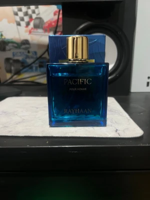 Pacific Pour Homme parfym Rayhaan - Snygg parfym från Rayhaan, Pacific Pour Homme. Flaskan är fyrkantig i blått glas med guldfärgat lock och detaljer. Kommer i matchande blå förpackning med gulddetaljer. Perfekt för dig som gillar stilrena och moderna dofter.
