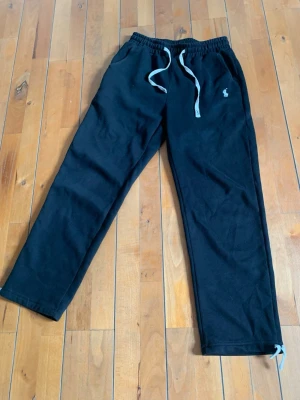 Svarta raka mjukisbyxor från Ralph Lauren - Snygga svarta mjukisbyxor från Polo Ralph Lauren med dragsko i midjan och två sidofickor. Byxorna har en broderad logga på låret och är tillverkade i mjukt material som passar perfekt för chill dagar. Klassisk rak passform och ribbad midja.