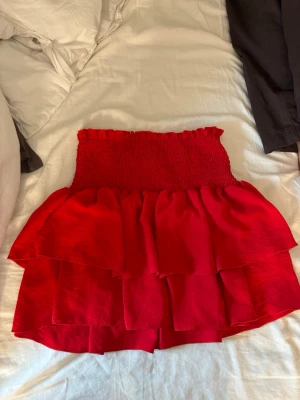 Röd volangkjol - Säljer en röd kjol med flera volanger Kjolen har en kort modell och är perfekt för dig som vill sticka ut med en färgstark look. Passar till både sneakers och boots för en trendig outfit.