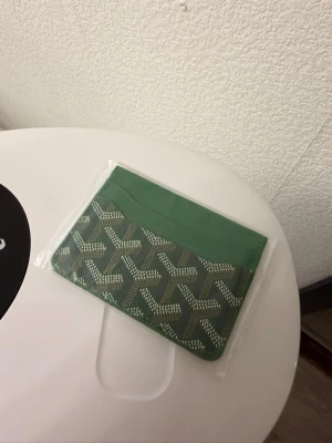Grön kortfodral  - Snyggt och stilrent kortfodral i grön färg med klassiskt mönster och logotyp. Fodralet är tillverkat i läder och har flera fack för kort. Perfekt för dig som vill ha något exklusivt och trendigt.