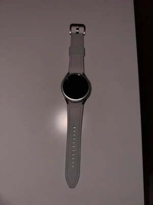 Vit Samsung Galaxy 6 smartklocka - Snygg vit Samsung Galaxy 6 smartklocka med rund urtavla och silikonarmband. Klockan har en stilren design med silverfärgad roterbar ram runt displayen och justerbart spänne. Perfekt för dig som vill ha koll på notiser, träning och hälsa direkt på handleden.                 Priset är såklart diskuterbart