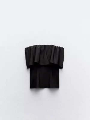 Svart tubtopp Zara - Trendig svart tubtopp från Zara med volang upptill och axelbandslös design. Perfekt för att skapa en cool och stilren look. Toppens material känns mjukt och stretchigt, vilket ger en bekväm passform.