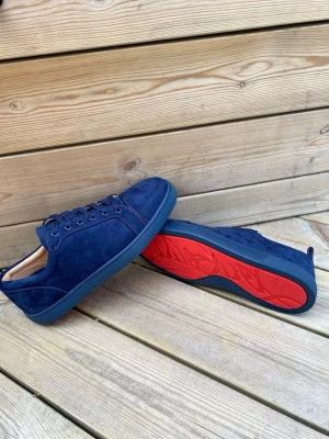 Mörkblå mockasneakers med röd sula - Snygga mörkblå sneakers i mocka med matchande blå snören och yttersula. Insidan är ljusbeige och sulan har en cool röd undersida med mönster. Perfekta för dig som vill ha en stilren men ändå unik look.