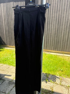 Svarta kostymbyxor  - Snygga svarta kostymbyxor med hög midja och raka ben. Byxorna har pressveck framtill och bälteshällor i midjan. Perfekta för en stilren och klassisk look. Materialet känns mjukt och följsamt.