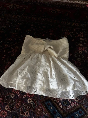Vit virkad och broderad tubtopp Zara - Supersöt vit tubtopp med virkad överdel och twistad detalj framtill. Nedre delen är i broderad bomull med blommönster och volang, vilket ger en romantisk vibe. Perfekt för varma dagar och sommarhäng. Från Zara 