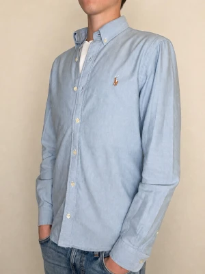 Ralph Lauren skjorta - Säljer en väldigt schysst Ralph Lauren skjorta som passar perfekt nu till sommaren, även när det är mer uppklätt. Färgen är blå och passformen är slim fit. Storleken är M och skjortan är gjord av bomull, en så kallad oxfordskjorta. Skicket är väldigt bra, det finns inga skavanker. Nypriset på denna är cirka 1800kr, men jag säljer för endast 399kr. Kontakta mig vid minsta lilla fundering och prisförslag!