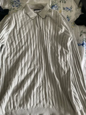 Ljusgrå stickad tröja med dragkedja - Snygg ljusgrå stickad tröja från ASOS DESIGN med ribbat mönster, krage och dragkedja framtill. Tröjan har långa ärmar och ribbade muddar vid ärmslut och nederkant. Perfekt för en stilren och avslappnad look.