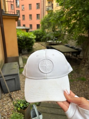 Vit keps från Stone Island - Snygg vit keps från Stone Island med broderad logotyp framtill. Klassisk böjd skärm och justerbar rem bak. Tillverkad i bomull för en bekväm och luftig känsla. Perfekt accessoar för en clean och stilren look.