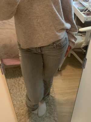 Grå bootcut jeans med fickdetaljer - Säljer ett par grå jeans med utsvängda ben och snygga fickdetaljer bak med knappar. Jeansen har låg midja. Passar perfekt till en avslappnad stil och är lätta att matcha med olika tröjor.