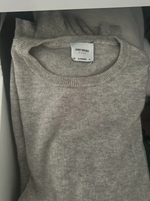 Ljusgrå cashmere-tröja John Henric - Ljusgrå stickad tröja från John Henric i 100% cashmere. Tröjan har rund hals, långa ärmar och ribbade muddar vid ärmslut och nederkant. Enkel och klassisk design som passar till många olika stilar.