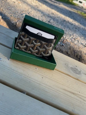  svart kortfodral i läder - Snyggt svart kortfodral  med det klassiska mönstret i vitt och beige. Tillverkat i läder och har flera fack för kort. Kommer i original grön ask. Perfekt för dig som vill ha en exklusiv och stilren accessoar.