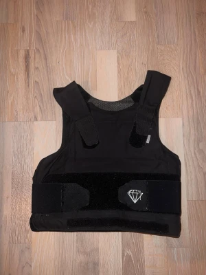 Skyddsväst RPS1/HG1/A - Marknadens lättaste väst som tar kaliber 9 mm! Komfortabel skottsäker skyddsväst med hög skyddsnivå i 360° runt kroppens vitala organ. Utvecklad för Polis, Väktare och Ordningsvakt. Västens absorberar fukt och håller dig sval och torr under hela ditt arbetspass. Skyddspanelerna överlappar varandra och ger dig ett fullt skydd runt om hela kroppen. Västen garanterar penetrationsskydd mot helmantlad 9 x 19 mm och .44 Magnum halvmantlad ammunition. Även stick & skärande samt emot kanyler & syl. 