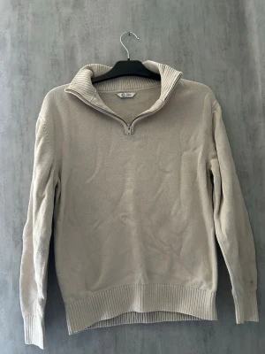 Beige stickad tröja med halv dragkedja - Snygg beige stickad tröja från C&A med halv dragkedja och hög krage. Tröjan har långa ärmar och ribbade muddar vid ärmslut och nederkant. Perfekt för lager på lager och enkel att matcha med olika outfits.