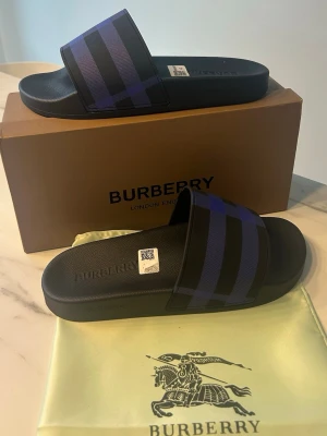 Burberry sandaler med blått rutmönster - Feta burberry slides i en unik färg storlek 42. De kommer med box och dustbsg och är oanvända. Perfekta inför sommaren. Pris kan alltid diskuteras.