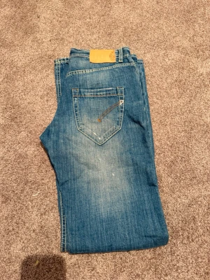 Blå raka jeans med slitningar, DunDup - Säljer ett par blå jeans med raka ben och snygga slitningar på framsidan. Jeansen har klassisk femficksdesign och kontrastsömmar. Perfekta för en avslappnad och trendig look.  Stl 31-34 kan va nån större eller mindre 