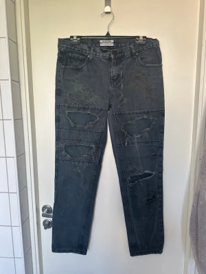 Grå slitna jeans från One Teaspoon W28 - Säljer ett par grå jeans från One Teaspoon med flera stora slitningar och hål på benen. Jeansen har klassisk femficksmodell, raka ben och är tillverkade i denim. Perfekta för en edgy och avslappnad stil.