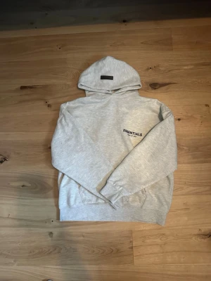 Grå essentials hoodie - En nästan helt ny grå hoodie från essentials som är snygg och stilren, och perfekt för lite kallare sommardagar och lite varmare vinterdagar, är lite oversized!! Kom med frågor som besvaras snällt.