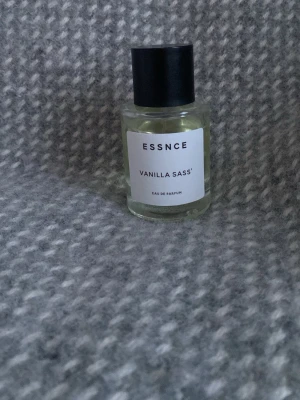 ESSNCE Vanilla Sass' Eau de Parfum - ESSNCE Vanilla Sass' Eau de Parfum i en stilren, genomskinlig glasflaska med svart lock. Doften har en tydlig vaniljkaraktär och flaskan har en minimalistisk vit etikett med svart text. Perfekt för dig som gillar söta och fräscha dofter. 