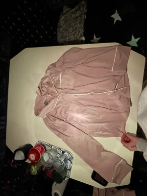 Rosa pyjamas med vita detaljer - Mysig tvådelad pyjamas i ljusrosa med vita passpoaler. Skjortan har knappar framtill och en bröstficka, byxorna har resår i midjan och raka ben. Byxorna är mera bagy Perfekt för chillkvällar hemma och riktigt skön mot huden.