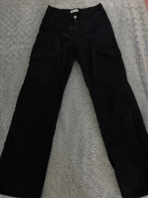 Svarta cargobyxor från Zara - Säljer ett par svarta cargobyxor från Zara med raka ben och stora fickor på sidorna. Byxorna har knapp och dragkedja framtill samt klassisk cargostil. Perfekta för en avslappnad och trendig look.