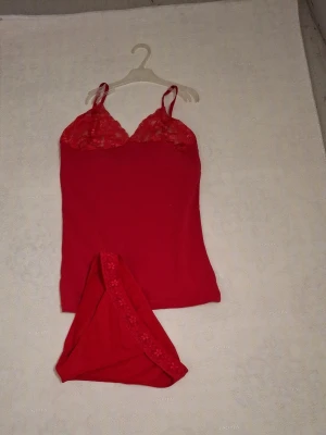Rött underklädesset med spetsdetaljer - Säljer ett rött underklädesset som består av ett linne och matchande trosor. Trosorna har fina spetsdetaljer och små blommor längs kanten. Materialet känns mjukt och stretchigt, perfekt för en bekväm känsla. Perfekt för dig som gillar färgstarka och feminina underkläder.