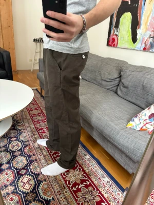 Bruna chinos från Elvine - Snygga bruna chinos från Elvine med raka ben och klassisk passform. Byxorna har två bakfickor med knappdetalj och bälteshällor i midjan. Tillverkade i ett mjukt och slitstarkt bomullsmaterial som känns bekvämt hela dagen.