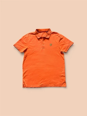 Orange pikétröja från Lyle & Scott - Snygg orange pikétröja från Lyle & Scott med klassisk krage och knappslå framtill. Tröjan har korta ärmar och den ikoniska loggan broderad på bröstet. Perfekt för en avslappnad men ändå stilren look.