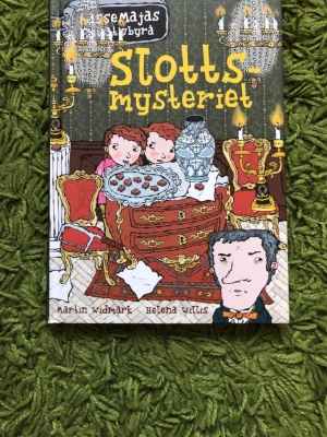 LasseMajas Detektivbyrå: Slottsmysteriet - En färgglad och illustrerad bok ur serien LasseMajas Detektivbyrå, skriven av Martin Widmark och illustrerad av Helena Willis. Omslaget har gröna, röda och gula toner med tecknade figurer och slottsmiljö. Perfekt för dig som gillar mysterier och spännande äventyr.