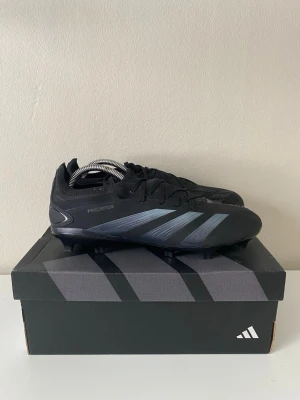 Adidas Predator svart fotbollssko (PRO) - Snygga svarta Adidas predator. Skorna har snörning, låg profil och dobbar för spel på gräs och konstgräs .Tillverkade i syntetmaterial för bra grepp och kontroll på planen. Använda en gång, säljer för att dem är för små. 