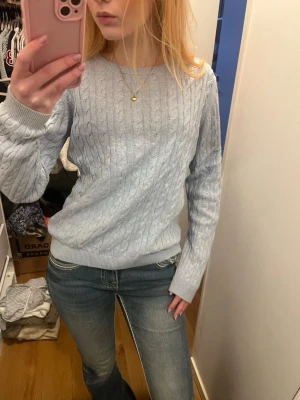 Ljusblå kabelstickad tröja - Ljusblå kabelstickad tröja med rund halsringning och ribbade muddar vid ärmslut och nederkant. Tröjan har en klassisk, avslappnad passform och är perfekt för lager på lager. Materialet ser mjukt och bekvämt ut, perfekt för kyligare dagar.