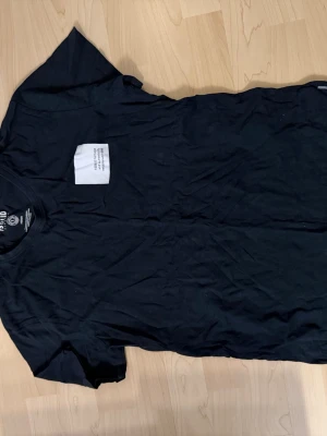 Svart t-shirt från Solid Denmark - En svart t-shirt från Solid Denmark med klassisk passform och rund hals. Tillverkad i mjuk bomull och har en liten vit patch med text på bröstet som ger en clean och modern vibe. Perfekt till jeans eller shorts.