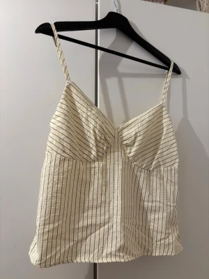 Randigt linne med smala axelband - Snyggt vitt linne med tunna svarta ränder och smala axelband. Den är köpt i storlek M men har liten i storlek så passar S.