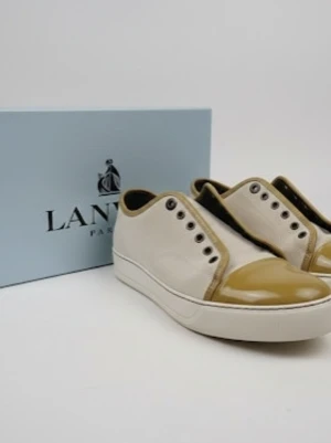 Lanvin Cap-Toe Sneakers - Exklusiva Lanvin Cap-Toe Sneakers i nyskick ​Passa på att förvärva en av modevärldens mest ikoniska sneakermodeller. Dessa Lanvin DBB0 kombinerar tidlös elegans med en modern twist, tack vare den snygga kontrasten mellan den ljusa ovandelen och den olivgröna tån i lackat läder. ​Detta är den perfekta skon för dig som vill ha en avslappnad men ändå extremt välklädd look som fungerar lika bra till kostymbyxan som till ett par råa jeans. ​Detaljer: ​Märke: Lanvin Paris. ​Modell: Cap-Toe Low Top. ​S