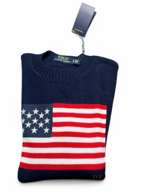 Mörkblå stickad tröja Polo Ralph Lauren - Mörkblå stickad tröja från Polo Ralph Lauren med amerikansk flagga i rött, vitt och blått på bröstet. Tröjan har rund halsringning och ribbstickade muddar. Perfekt för dig som gillar klassisk och sportig stil.
