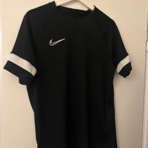 Svart Nike sporttröja med vita detaljer - Snygg svart sporttröja från Nike med vita detaljer på ärmarna och en vit Nike-logga på bröstet. 