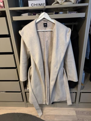 Beige kappa från Zara med skärp - Stilren beige kappa från Zara med bred krage och knytskärp i midjan. 