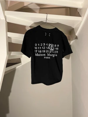Maison Margiela svart t-shirt - Svart t-shirt från Maison Margiela med den ikoniska loggan på ryggen. Perfekt för dig som vill ha en stilren och skön tröja till sommaren. Skick 10/10 knapp använd. Skulle passa 160-165 beroende på. 